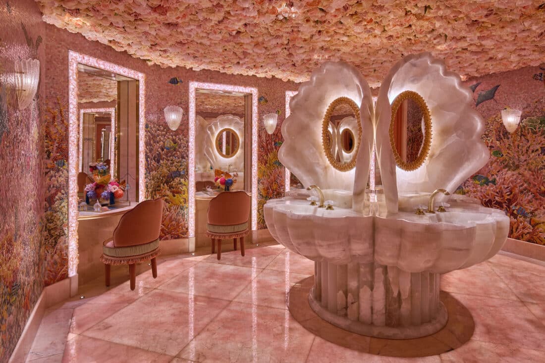 The bathrooms feature shell-shaped onyx sinks, vibrant coral reef visuals, and a floral ceiling that completes the venue’s surreal, underwater allure